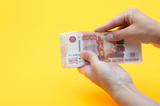 Two hands holding a crustacean of five thousandth Russian rubles on a yellow background - Фото, изображение