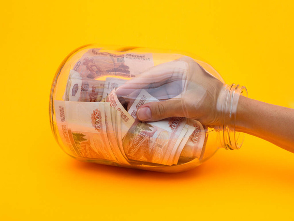 Hand klom in een glazen pot vol vijfduizendste biljetten - Foto, afbeelding
