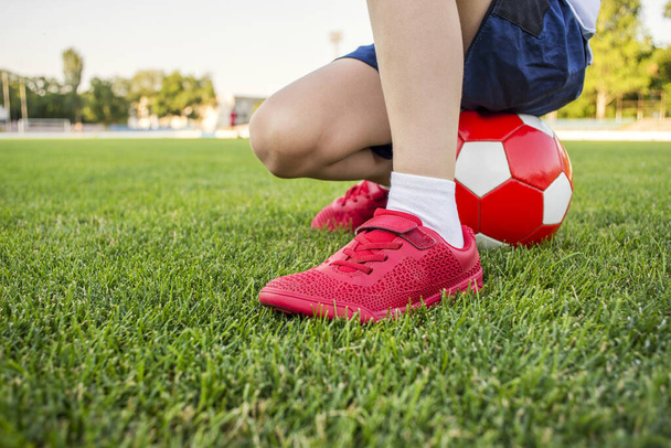 A child is sitting on a soccer ball on the grass of stadium's field. Training and sports for children concept. - Photo, Image