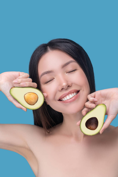 Happy woman holding two pieces of ripe avocado - 写真・画像