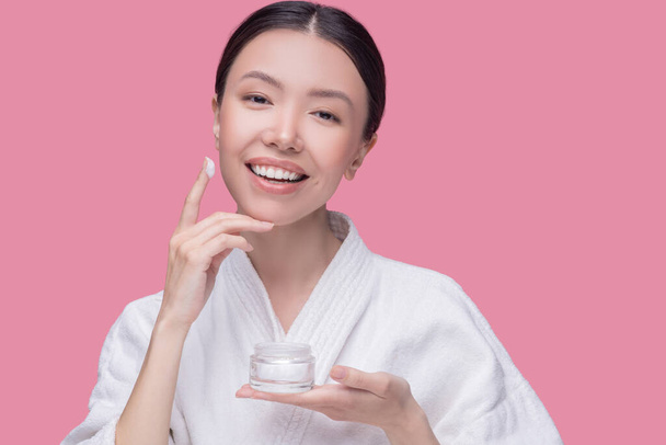 Smiling woman applying facial cream to her skin - Fotó, kép