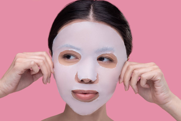Woman applying textile skincare mask to her face - Fotoğraf, Görsel