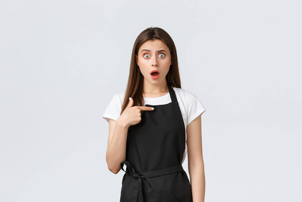 Grocery store employees, small business and coffee shops concept. Shocked and questioned cute female cafe worker in black apron pointing herself with worried expression - Photo, Image