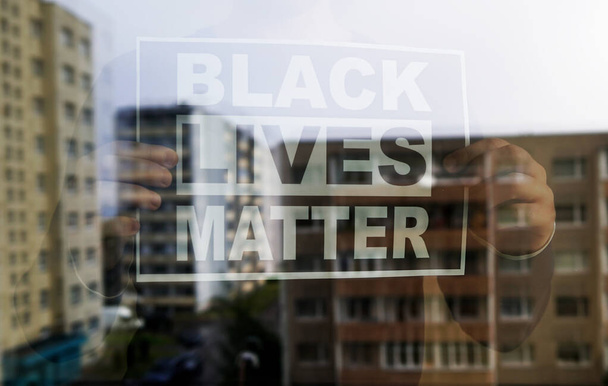Un uomo con il cartello "Black lives matter" dietro la finestra durante la quarantena di Covid-19. - Foto, immagini