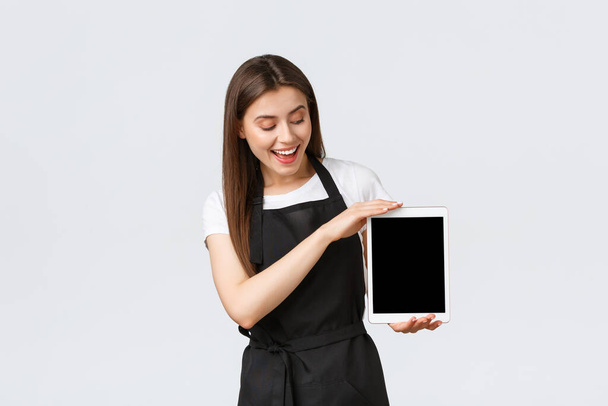 食料品店の従業員、中小企業やコーヒーショップのコンセプト。デジタルタブレット画面を示す陽気なフレンドリーな女性カフェ労働者は、オンライン注文アプリを表示します。バリスタが新しいメニューを紹介 - 写真・画像