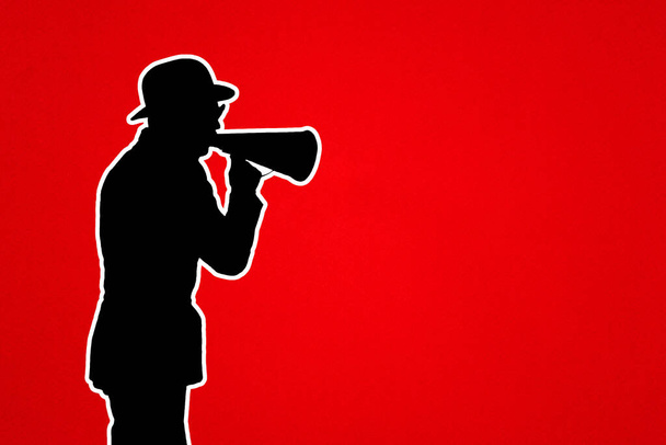 空間のコピーを持つ赤い背景にメガホンを持つ男。帽子を被った男とスピーカーのシルエット。情報、ニュース、注目を集める、広告の概念. - 写真・画像