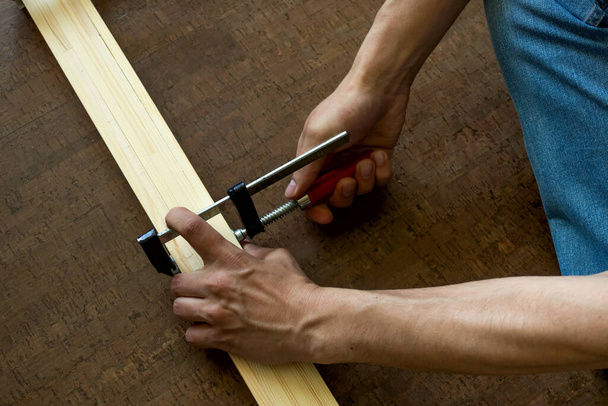 Mens hands fasten the clamp to the wooden rails, making a measurement before cutting. Repair concept - Foto, imagen