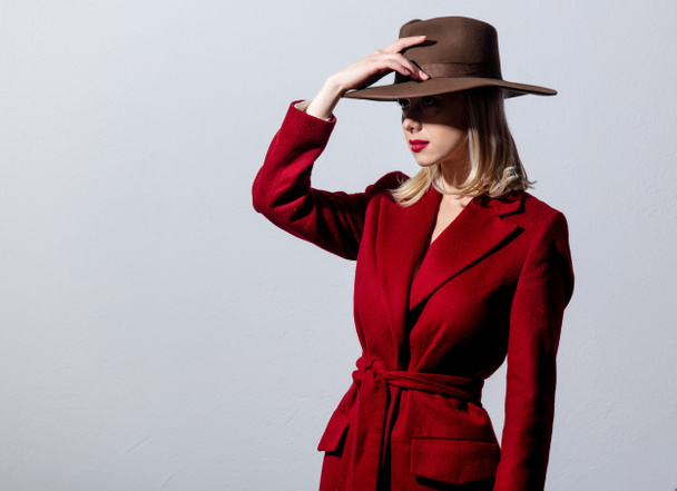 Blonde girl in red coat and vintage hat on grey background. Image in noir style  - Fotografie, Obrázek