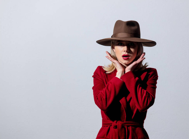 Блондинка в красном пальто и винтажной шляпе на сером фоне. Изображение в стиле нуар
  - Фото, изображение