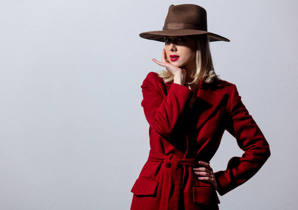 Blonde girl in red coat and vintage hat on grey background. Image in noir style  - Фото, изображение