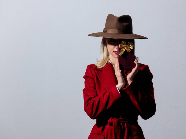 Blonde girl in red coat and vintage hat with candy box on white background - Fotó, kép