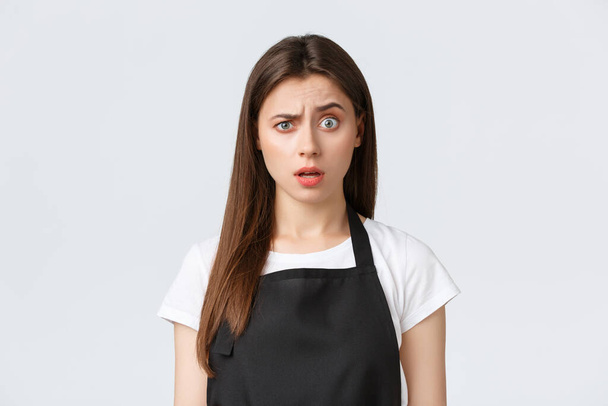 Employees, job employment, small business and coffee shop concept. Confused woman cashier, barista looking at something strange, raise eyebrow doubtful, stand white background - Photo, Image