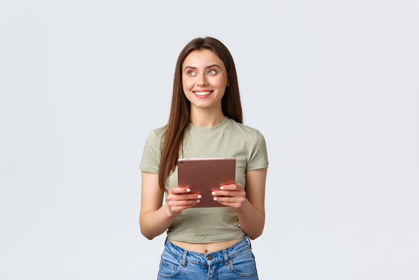 Fashion and beauty, lifestyle and shopping concept. Dreamy attractive, stylish woman looking top left corner with pleased smile while using digital tablet, making online order - Photo, Image