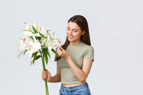 Улыбающаяся красавица-кавказка получает цветы из цветочного магазина, радуясь букету белых лилий. Девушка мечтательный трогательный лист и думать о парне, который сделал романтический жест
 - Фото, изображение