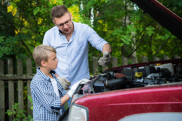 Vader leert zijn zoon hoe hij de auto moet repareren - Foto, afbeelding
