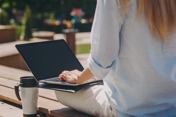 La dama de negocios habla por teléfono. Una joven mujer de negocios está trabajando con un ordenador portátil en una camisa azul en la calle en un parque bajo el sol! Concepto empresarial
 - Foto, Imagen
