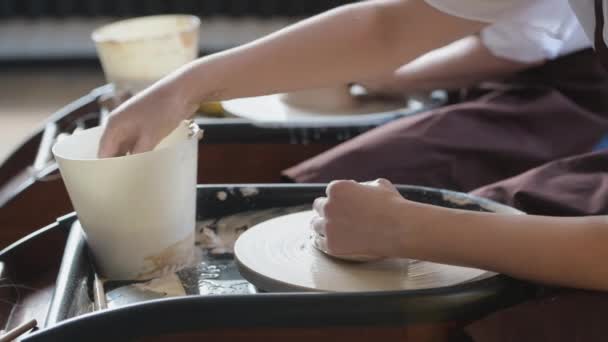 Detailní záběr Potter ruce v akci tvarování syrové hliněné hlíny pomocí vody na pohybující se hrnčířské kolo v keramické dílně. - Záběry, video
