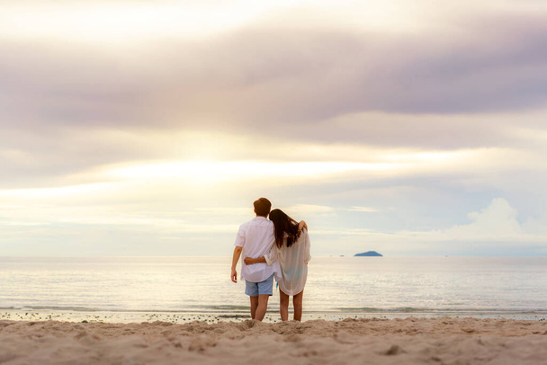 Romantic Asian young couple in love hugging and looking togerther and laughing at sunset on beach to happy while they honeymoon. Summer Vacation and Holidays concepts. - Foto, Imagen