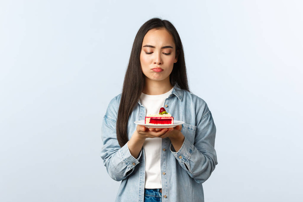 Social distancing lifestyle, covid-19 pandemic, celebrating holidays during coronavirus concept. Reluctant and depressed gloomy asian girl looking displeased at birthday cake, feel distressed - Foto, afbeelding