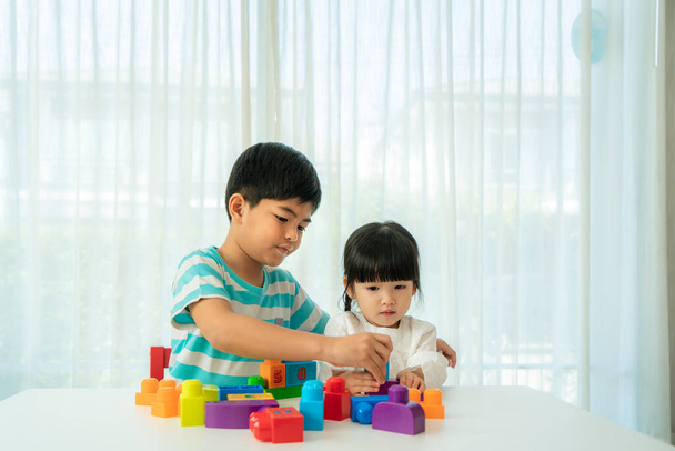 Asiatische süße Bruder und Schwester spielen mit einem Spielzeug Block Designer auf dem Tisch im Wohnzimmer zu Hause. Konzept der Bindung von Geschwistern, Freundschaft und Lernen durch Spielaktivitäten für die Entwicklung von Kindern. - Foto, Bild