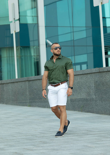 Confident handsome man in sunglasses and shirt over city background. Men's beauty, fashion. Outdoor portrait. - 写真・画像
