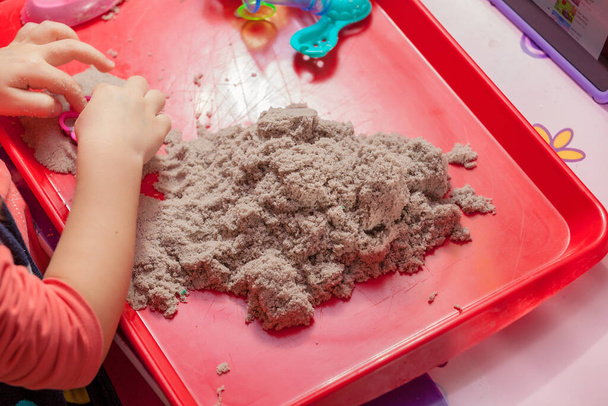 kleine Hände, die mit kinetischem Sand und Schimmelpilzen auf der roten tra spielen - Foto, Bild
