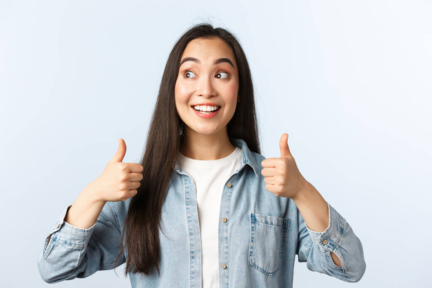 Lifestyle, people emotions and beauty concept. Excited happy asian woman peeking left and smiling broadly as showing thumbs-up in approval, recommend cool promo, give advice - Photo, Image