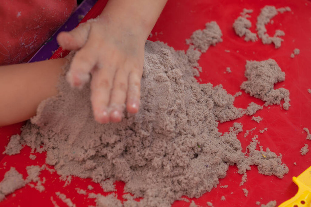 little hands playing with kinetic sand and molds on the red tray - Photo, Image