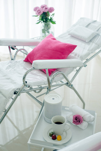 белый стул в спа-салоне с розовой подушкой, розы и кофе со сладостями - Фото, изображение