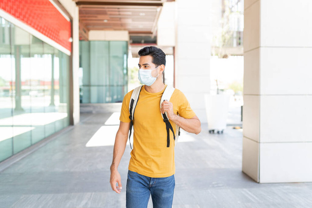 Lateinischer junger Mann mit Gesichtsmaske läuft während Coronavirus-Ausbruch auf Fußweg in der Stadt - Foto, Bild