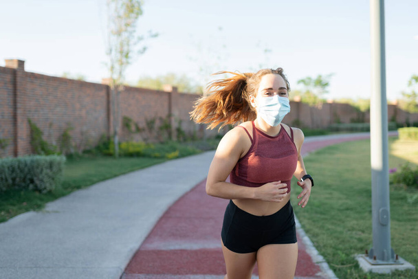 Athletic young woman wearing face mask while jogging in park - Photo, Image