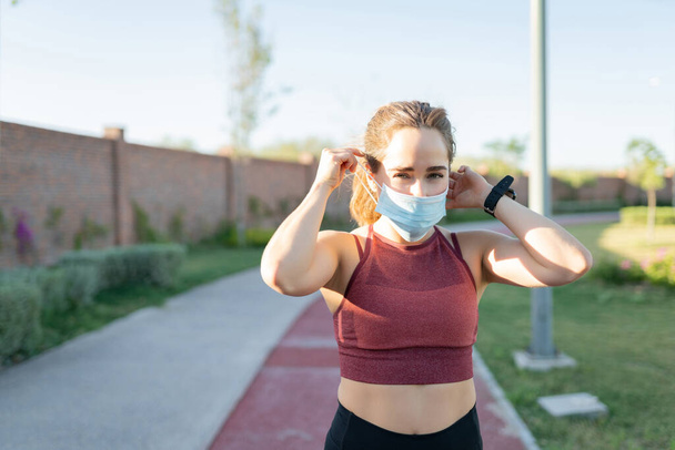 Sporty young woman wearing face mask while exercising in park - Photo, Image