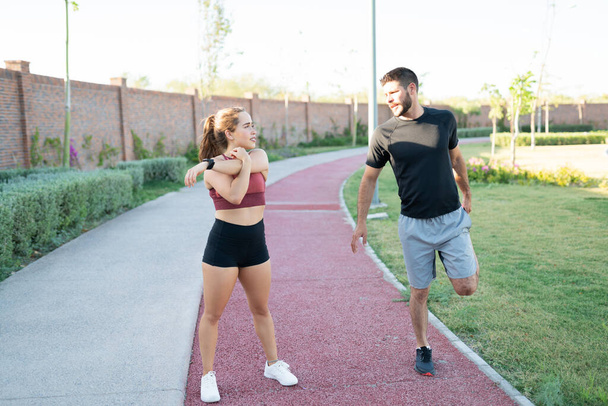 Deportivo joven hombre y mujer hablando mientras hace ejercicio de calentamiento en el parque
 - Foto, Imagen
