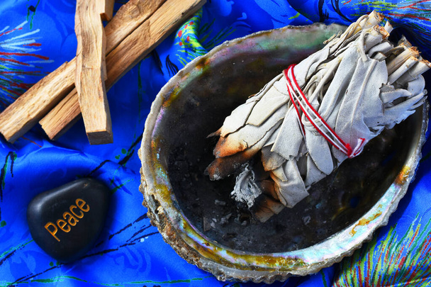 Y la imagen de paquetes de salvia blanca en una concha de abulón sobre un fondo de seda azul brillante
.  - Foto, Imagen