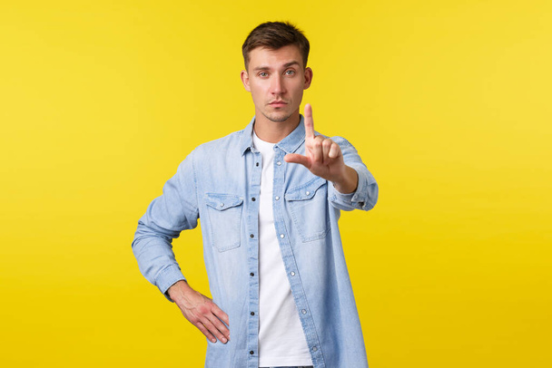 Lifestyle, people emotions and summer leisure concept. Serious gay man in casual outfit, shaking finger in prohibition, disapprove and trying stop person, give restriction over yellow background - Photo, Image