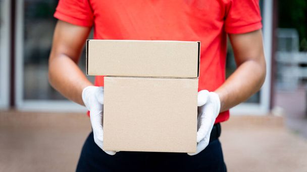 Близько до доставки людина тримає посилки і коробку перед будинком клієнта, щоб доставити онлайн-замовлення покупок під час пандемії COVID-19. Особа доставки доставляє посилку
. - Фото, зображення