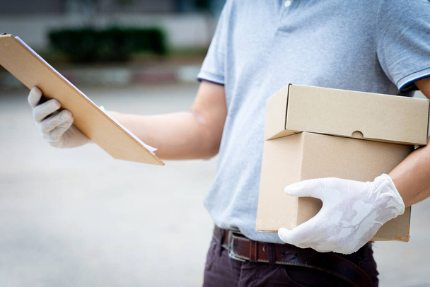 Close up of a delivery man holds parcels and box infront of customer's house to delivery online shopping order during COVID-19 pandemic. Delivery person delivers parcel post. - Foto, afbeelding