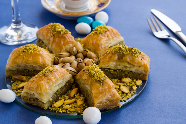 Traditional Turkish Pastry Dessert Baklava designed on glass plate at blue surface with cutlery set and candy.Feast concept. - Photo, Image