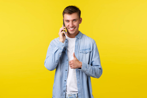 Technology, lifestyle and advertisement concept. Pleased good-looking man talking on phone, assure everything going well, showing thumbs-up to encourage you all good, making agreement while calling - Photo, image