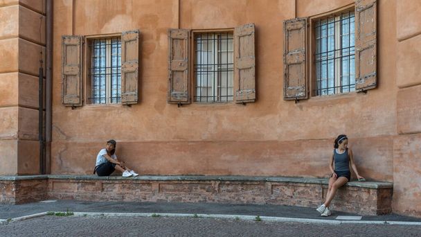 Moeder en dochter zitten op bakstenen bank voor een mooie terracota gepleisterde muur in Bologna Italië - Foto, afbeelding