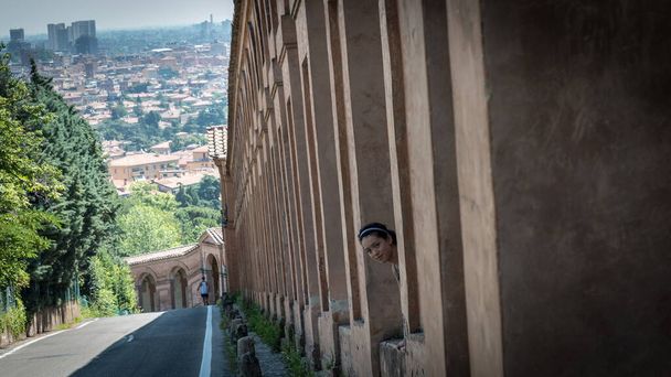 Teen with headband sticking her head out between columns of portico in Bologna Ιταλία - Φωτογραφία, εικόνα