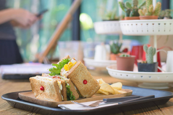 Клубный сэндвич с беконом - курица, яйцо, сыр, картофель и салат на деревянной столешнице на фоне кафе
. - Фото, изображение