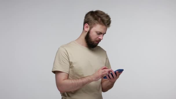 Omg, what is this? Bearded man looking at camera with disappointment, gesturing indignant expression after using mobile phone, dissatisfied with device and app. studio shot isolated on gray background - Video, Çekim