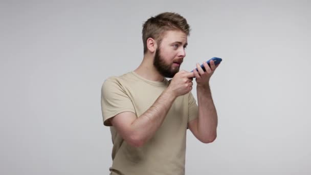 Virtual assistant. Cheerful bearded man recording message on mobile phone, talking to cellphone giving voice command to digital ai technology application. studio shot isolated on gray background - Filmmaterial, Video