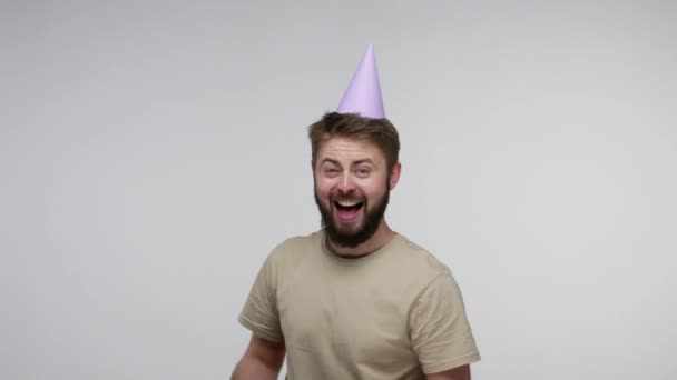 Amazed happy delighted bearded man with funny party cone hat showing wrapped gift box and laughing, excited about present, celebrating birthday anniversary. studio shot isolated on gray background - Metraje, vídeo