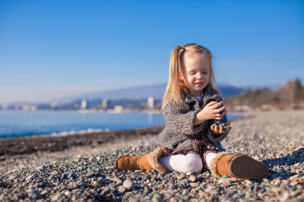 αξιολάτρευτο μικρό κορίτσι στην παραλία έχουν διασκέδαση σε ζεστή μέρα του χειμώνα - Φωτογραφία, εικόνα