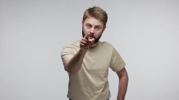 Hey you! Angry bearded guy noticing the guilty and pointing finger at camera, looking strict angry, dissatisfied with behavior, accusing for troubles. indoor studio shot isolated on gray background - Imágenes, Vídeo