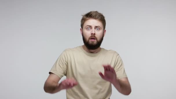 Scared bearded man walking back raising hands to defend against threat danger, afraid even look at phobia, hysterical panicking showing stop gesture. indoor studio shot isolated on gray background - 映像、動画