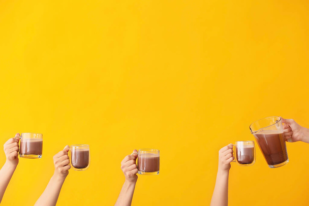 Manos con tazas de bebida de cacao caliente sobre fondo de color
 - Foto, Imagen