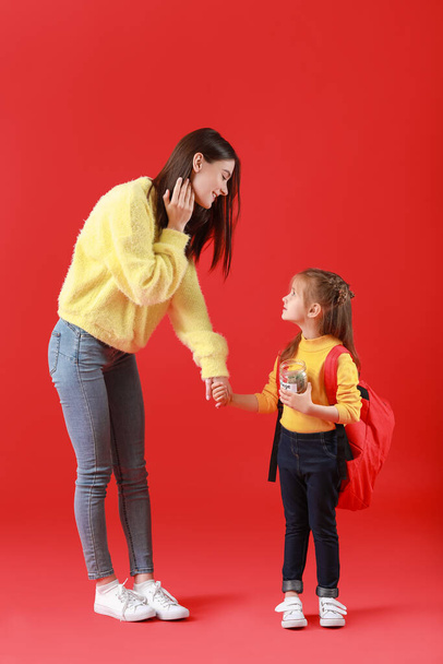 Klein meisje en haar moeder met besparingen voor onderwijs op kleur achtergrond - Foto, afbeelding